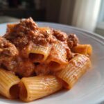 A close-up of a white bowl filled with Creamy High Protein Beef Pasta, featuring rigatoni noodles coated in a rich meat sauce.