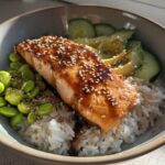 A delicious Crispy Salmon and Rice Bowl featuring a glazed salmon fillet, white rice, edamame, sliced avocado, and cucumber.