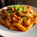 A close-up of Crock Pot Creamy Cajun Chicken Pasta served on a white plate and garnished with chopped green onions.
