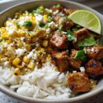 A delicious Easy Street Corn Chicken Bowl featuring rice, seasoned chicken, corn, crumbled cheese, and cilantro, topped with a lime wedge.