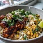 A close-up of an Easy Street Corn Chicken Bowl featuring seasoned chicken, corn, rice, crumbled cheese, and cilantro, garnished with a lime wedge.