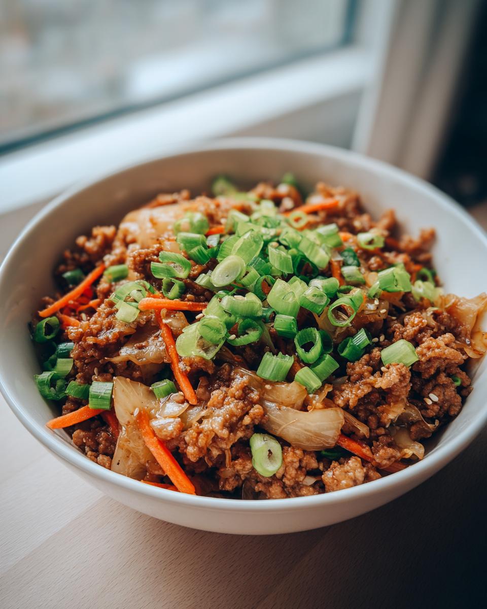 A close-up of a white bowl filled with Egg Roll in a Bowl, topped with fresh green scallions and sesame seeds.