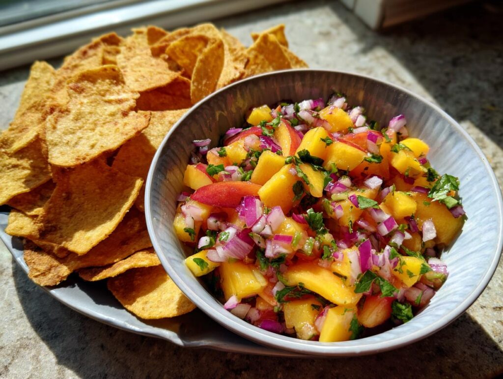 A bowl of fresh peach salsa with diced peaches, red onion, and cilantro, served with cinnamon chips.