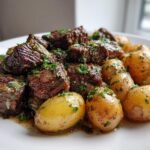 Close-up of juicy garlic steak bites piled high with tender baby potatoes, garnished with fresh parsley.