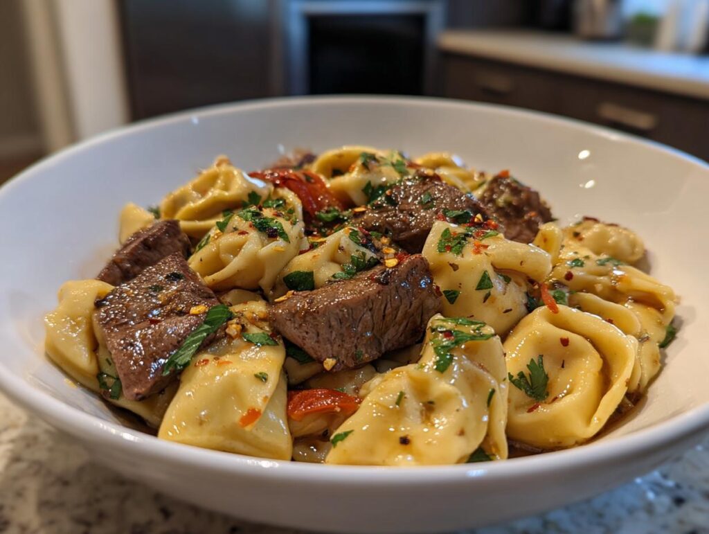 A close-up of a white bowl filled with Garlic Steak Tortellini, garnished with fresh parsley and red chili flakes.
