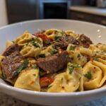 A close-up of a white bowl filled with Garlic Steak Tortellini, garnished with fresh parsley and red chili flakes.