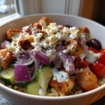 A vibrant bowl of Greek Chicken Bowls featuring grilled chicken, quinoa, cucumber, red onion, tomatoes, olives, and feta cheese.