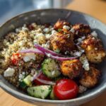 A bowl of Greek Chicken Bowls with quinoa, chicken, cucumber, tomatoes, red onion, and feta cheese.