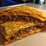 Close-up of a homemade ground beef crunchwrap cut in half, showing layers of seasoned ground beef and melted cheese.