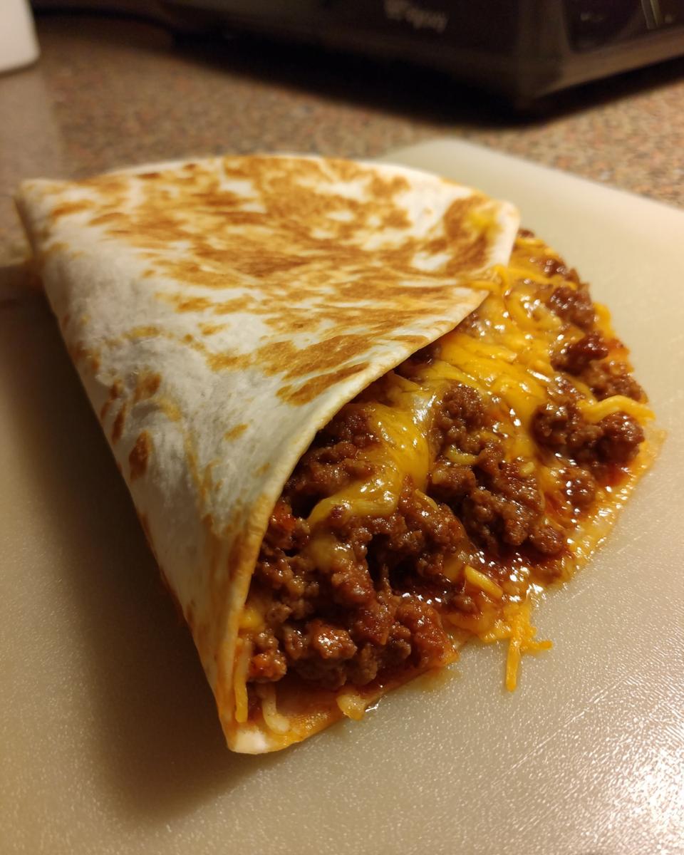 Close-up of a delicious homemade crunchwrap filled with seasoned ground beef and melted cheese.