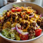 A delicious bowl of High-Protein Cheeseburger Bowls with ground beef, lettuce, tomatoes, onions, pickles, and melted cheese.