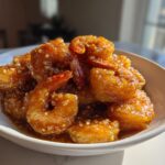 A bowl of glistening High-Protein Honey Garlic Shrimp coated in a sweet and savory sauce with sesame seeds.