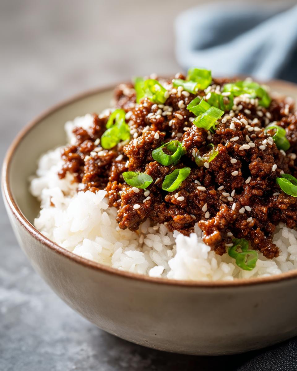 A close-up of a Korean beef rice bowl with seasoned ground beef, white rice, and green onions, topped with sesame seeds.