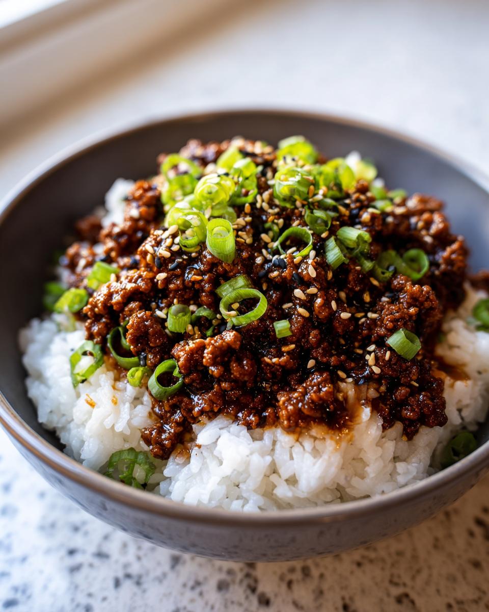 A close-up of a Korean Ground Beef Bowl, featuring seasoned ground beef over fluffy white rice, topped with green onions and sesame seeds.
