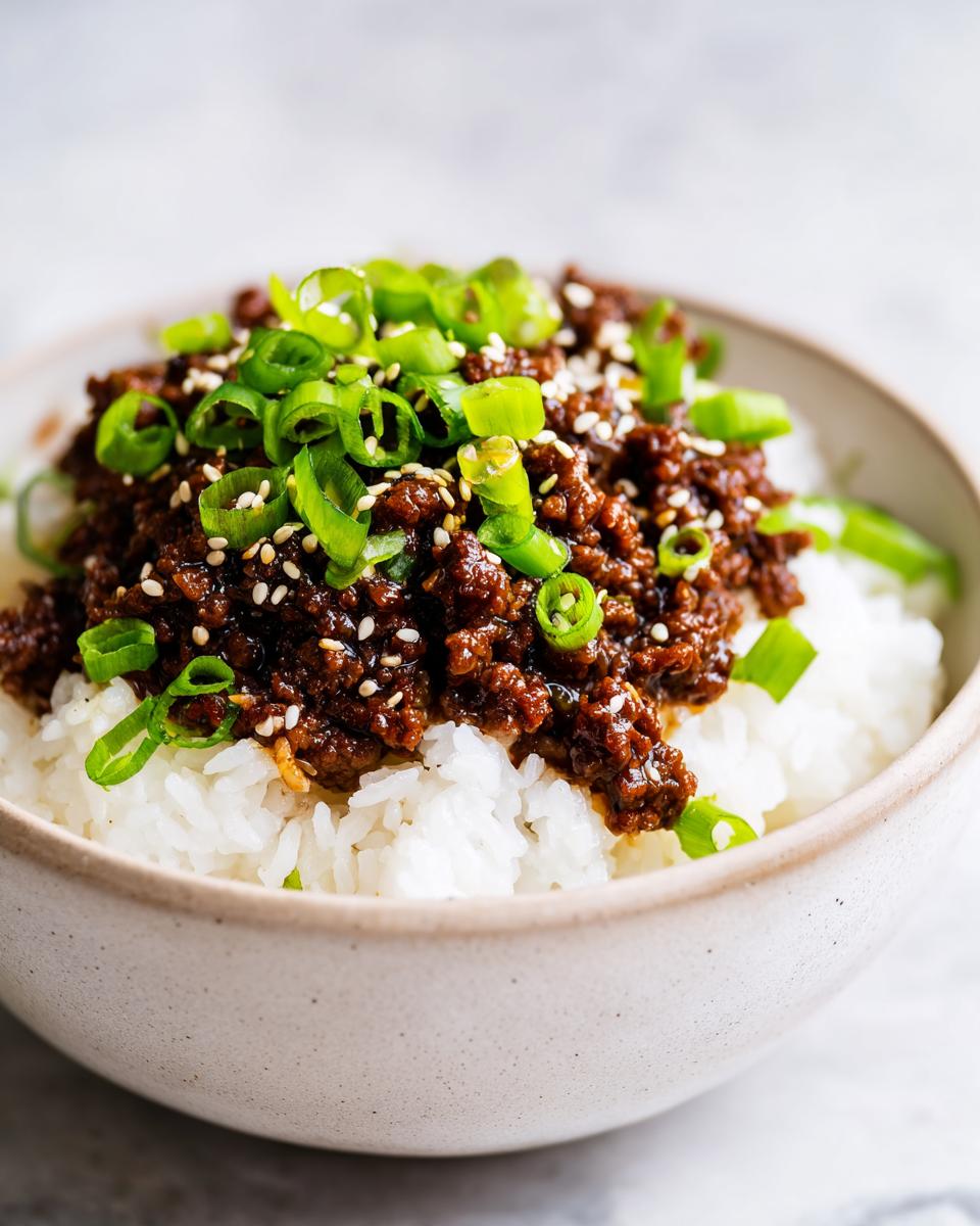 A close-up of a Korean Ground Beef Bowl, featuring seasoned ground beef over white rice, topped with chopped green onions and sesame seeds.