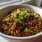 A bowl of Mongolian Ground Beef Noodles Recipe topped with green onions and sesame seeds.