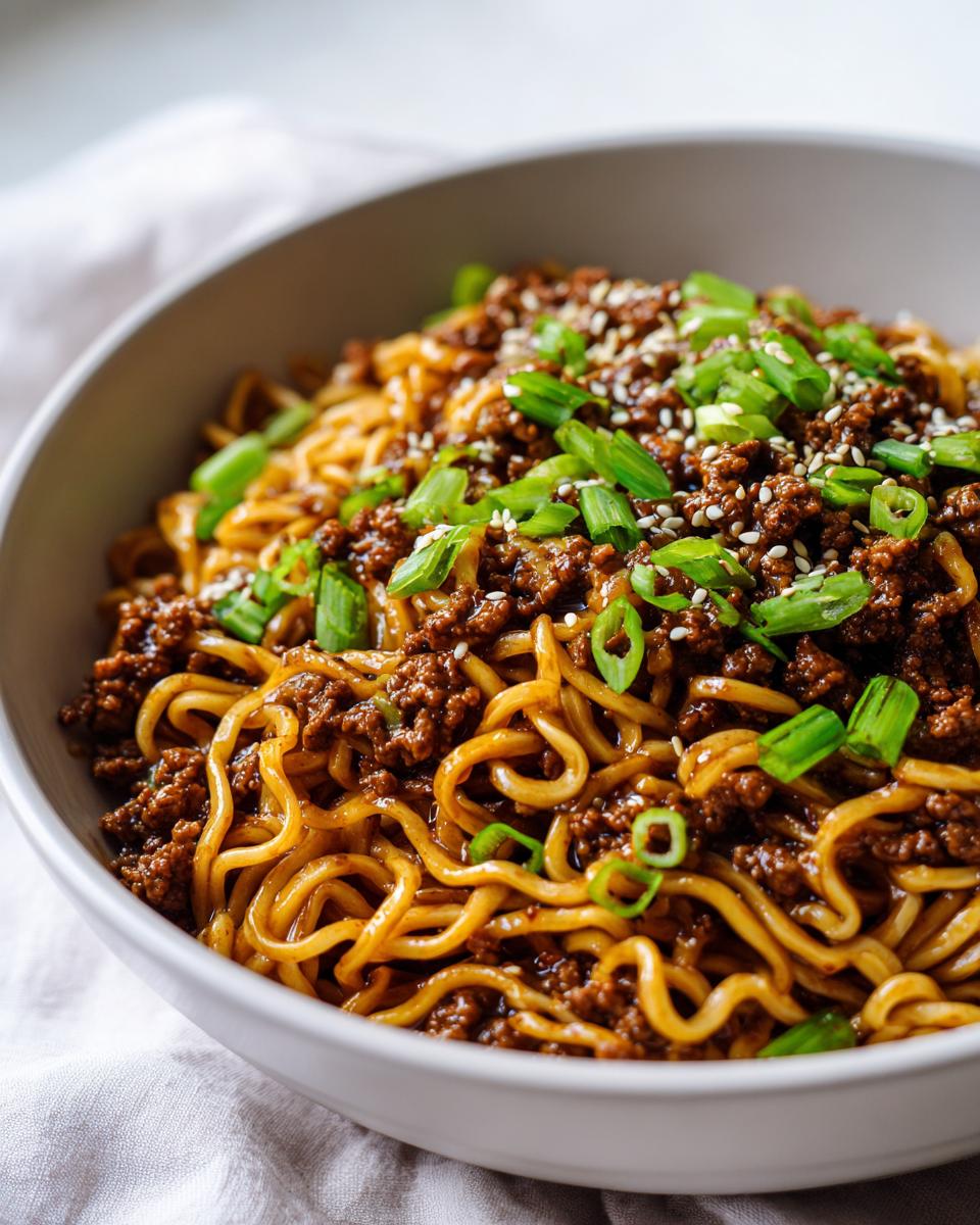 Close-up of a bowl of Mongolian Ground Beef Noodles, topped with sesame seeds and green onions.
