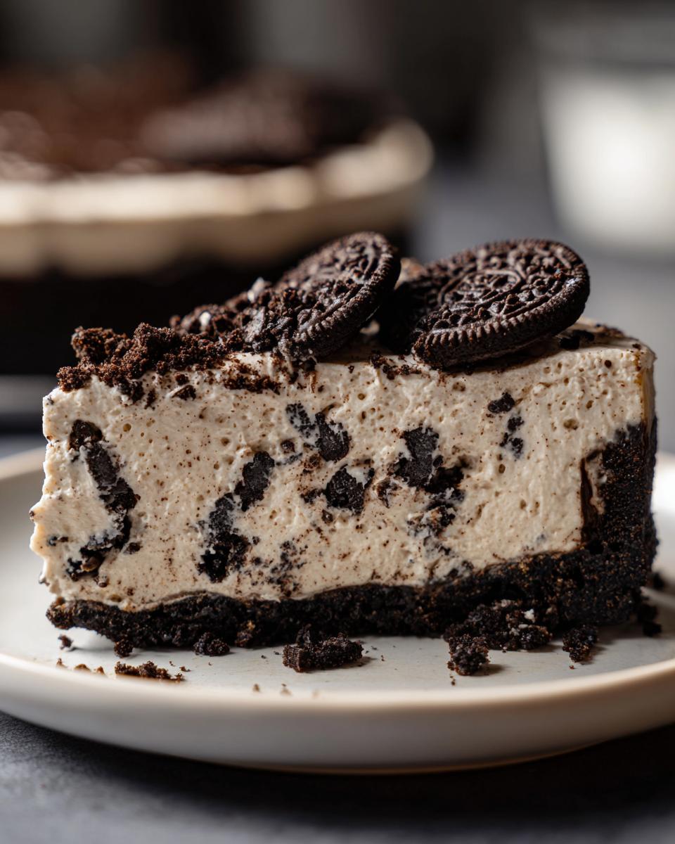 A slice of no-bake Oreo cheesecake on a plate, topped with Oreo cookies and cookie crumbs.