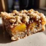 Close-up of a single peach crumble bar with a thick, buttery oat topping and juicy peach filling.