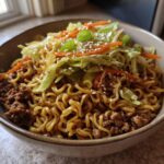 A close-up of a Potsticker Noodle Bowl with Pork & Cabbage Slaw, featuring noodles, ground pork, and fresh slaw topped with sesame seeds.