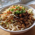 A close-up of a Potsticker Noodle Bowl with Pork & Cabbage Slaw, featuring thick noodles, savory ground pork, and fresh slaw.
