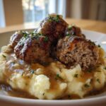A plate of Salisbury Steak Meatballs served over creamy Garlic Herb Mashed Potatoes, drizzled with gravy and garnished with parsley.