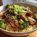A close-up of Spicy Garlic Chicken and Broccoli Noodle Bowls, featuring tender chicken pieces in a glossy sauce with vibrant broccoli florets and noodles.
